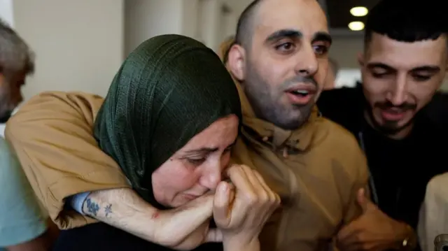 An emotional woman kisses the hand of a man in  a brown jacket