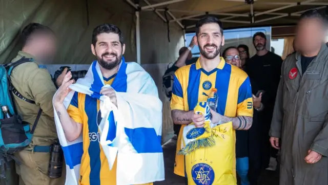 Two men in striped sports tops with israeli flags draped around their shoulders
