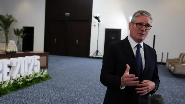 Starmer speaks to reporters in a white room with a blue carpet