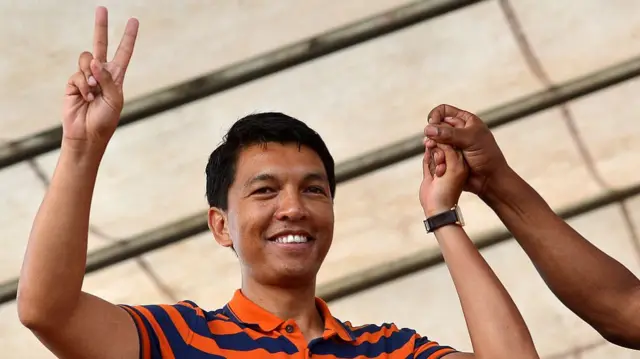 Andry Rajoelina makes the "peace" hand gesture while holding another person's hand aloft