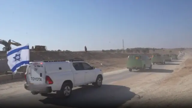 Convoy of green cars with number plates blurred, followed by a white car with an Israeli flag flying on it