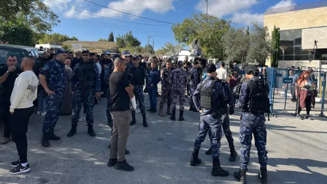 Crows of people, including some dressed in blue camo and security vests, gathered outside