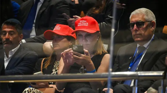 Two women sitting down wearing red caps