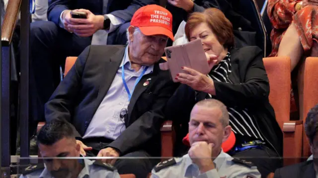 A man wears red Trump the Peace president as he sits in the audience section of the Knesset