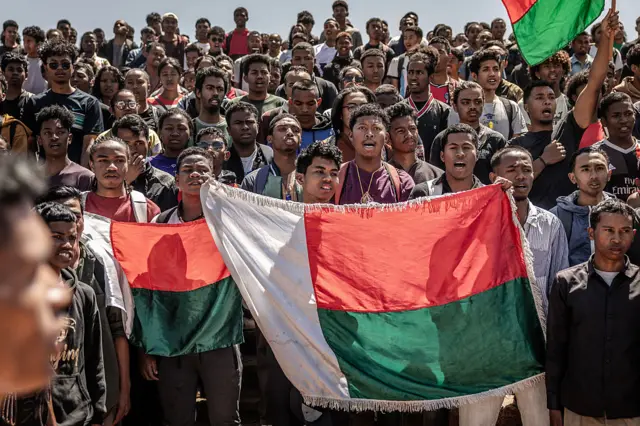 Students sing the national anthem while holding Malagasy flags as they gather to march toward a civil society rally at Ankatso University in Antananarivo, on October 13, 2025. Soldiers and security forces joined hundreds celebrating in Madagascar's capital on October 13, 2025, hours before President Andry Rajoelina was due to address the nation following weeks of protests and growing calls for his resignation. (Photo by Luis TATO / AFP) (Photo by LUIS TATO/AFP via Getty Images)