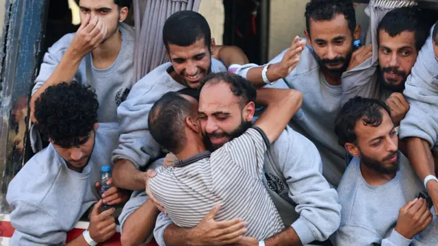 Men in grey sweatshirts hug each other and look visibly emotional