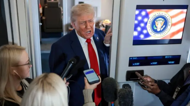 Donald Trump in darks suit addresses press pool inside Air Force One