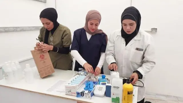 Three female medical staff in hijabs sorting the medical equipment on a table