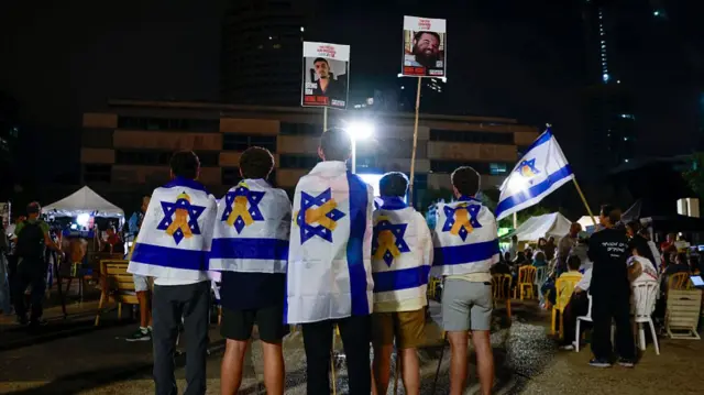 Israelis draped in Israeli flags decorated with yellow ribbons carry banners with photos of Israelis held hostage by Hamas