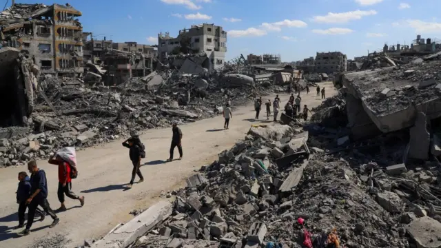 Palestinians walk past the rubble of destroyed buildings