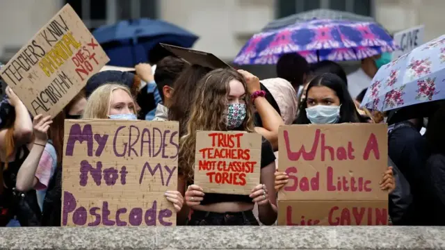 Students hold placards reading messages such as "My grades not my postcode"