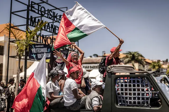 A woman waves a flag from the back of a pick-up truck.
