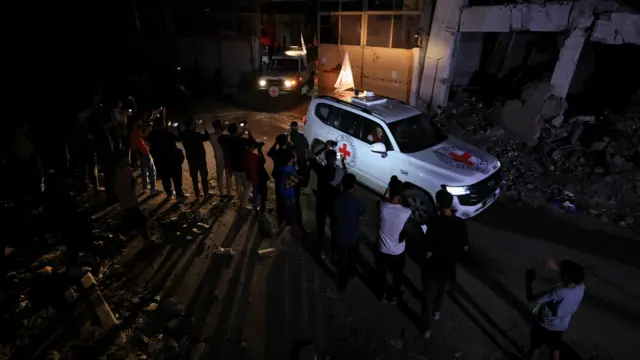 Red cross cars in compound surrounded by people