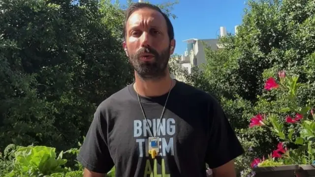 Daniel Lifshitz speaking from a garden in Tel Aviv wearing a t-shirt which says: "Bring them all home"