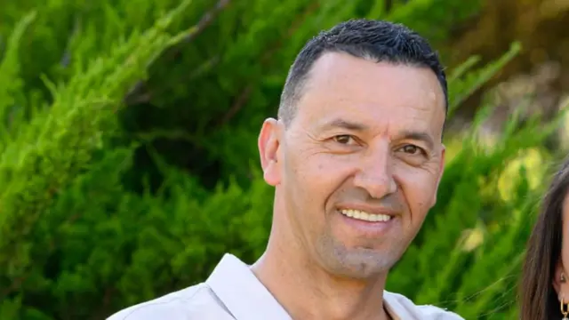 A man smiles iin front of some green bushes