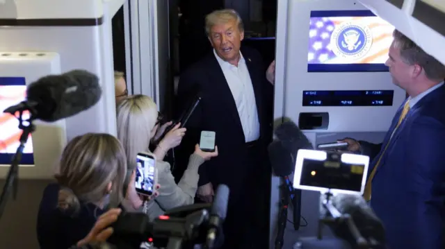 U.S. President Donald Trump speaks to the media aboard Air Force One after participating in a world leaders' summit on ending the Gaza war, amid a ceasefire between Israel and Hamas in Gaza, during a refueling stop on his way back to the US. Trump is surrounded by reporters holding microphones and cameras towards his direction