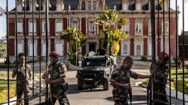 Four men in military fatigues open the gates of the presidential palace so a military vehicle can exit it