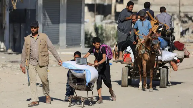 People push their belongings on a trolley while a donkey tows a trailer behind with people and possessions