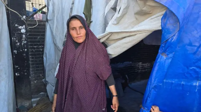 A woman in purple clothing stands by a blue tent
