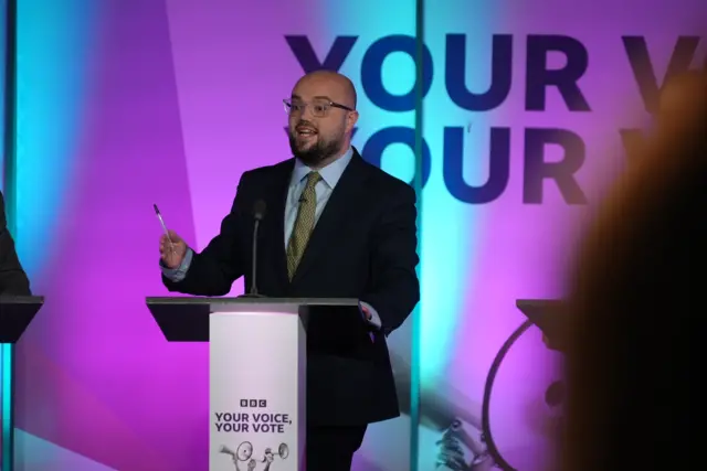 Llyr Powell on stage wearing a suit during the debate
