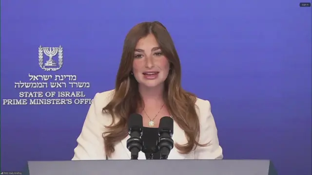 A woman with long hair stands at a podium