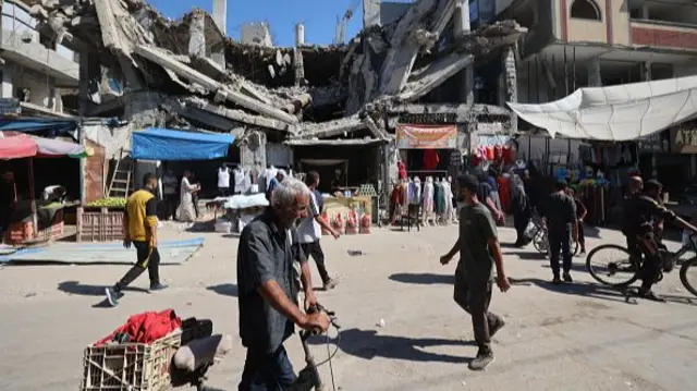 Palestinians walk past a destroyed building at a makeshift market in the Nuseirat refugee camp