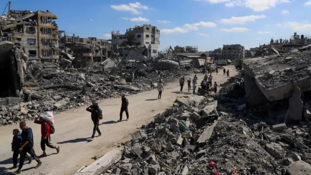Palestinians walk past the rubble of destroyed buildings