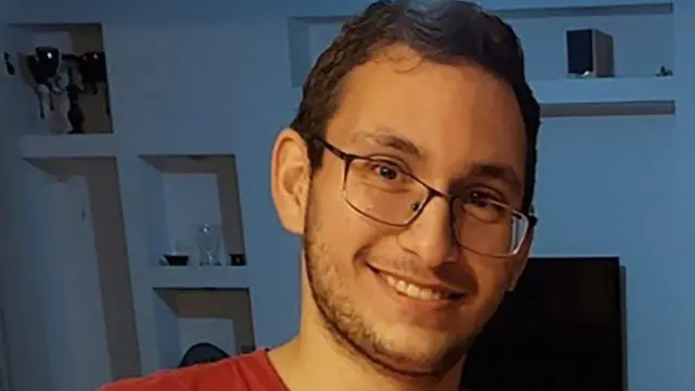 Tamir Nimrodi wearing a red t shirt and glasses, smiling into the camera