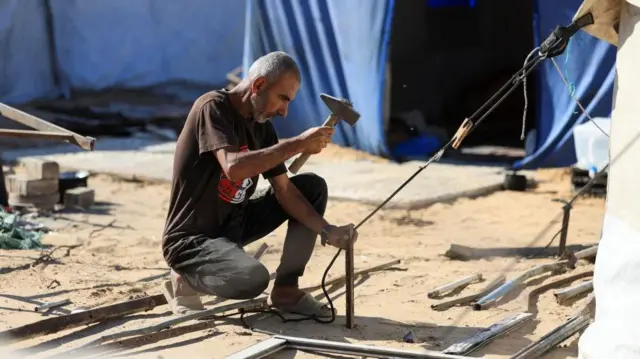 A man kneels down over a tent peg and hammers it into the ground