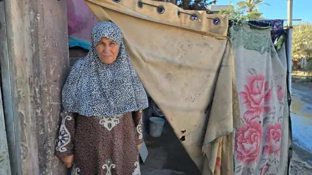 Woman in printed dress and hijab stands in front of a makeshift tent
