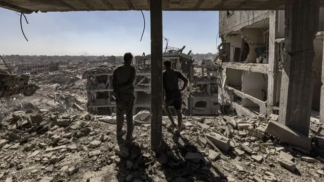 Two men inside a heavily damaged building observe the destruction around them
