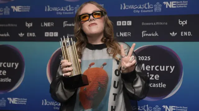 Emma-Jean Thackray arriving for the 2025 Mercury Music Prize awards show, posing with her nominee trophy