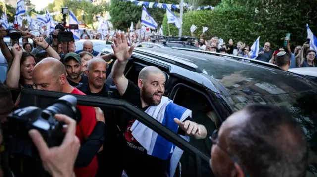 A man waves at a crowd as he gets into a black car