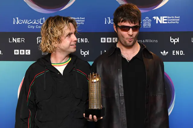 Fontaines DC members at the Mercury Prize 2025 ceremony holding a nominee's trophy