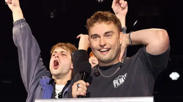 Sam Fender looking gobsmacked after winning the Mercury Prize, he has his hand behind his head and two friends are celebrating behind him