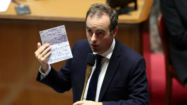 Lecornu stands and delivers a speech with his notes in one hand