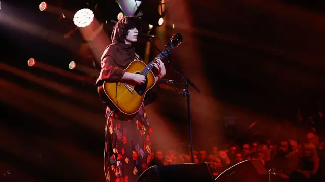 Singer Jacob Alon holds a guitar on stage at the Mercury Prize 2025