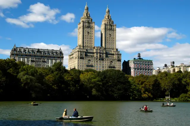 The San Remo Apartment building stands on Central Park West, behind people rowing on The Lake in Central Park, Manhattan, New York City. Autumn 2004.