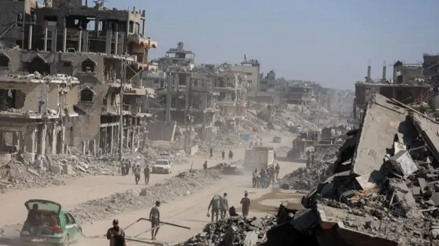 Palestinians walk past the rubble of destroyed buildings in Gaza City
