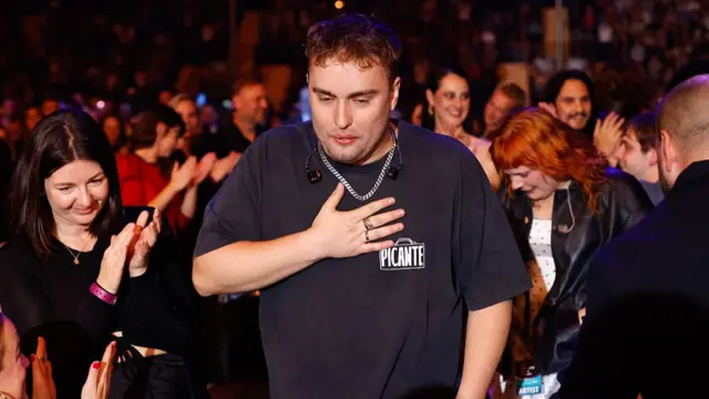 Fender stands with a hand on his chest as the audience around him applauds