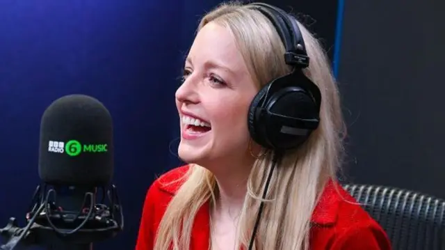 Radio 6 presenter Lauren Laverne laughing while speaking into a radio mic and wearing headphones