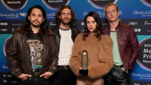 A group of four, three men and one woman, pose for the camera holding a cylinder-shaped award