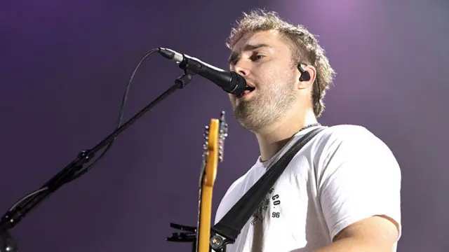 Sam Fender singing on stage with guitar