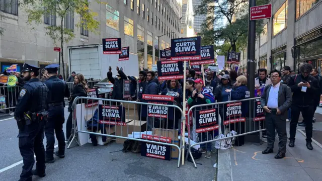 A group of people holding Curtis Sliwa signs stand in an enclosed area with police standing nearby