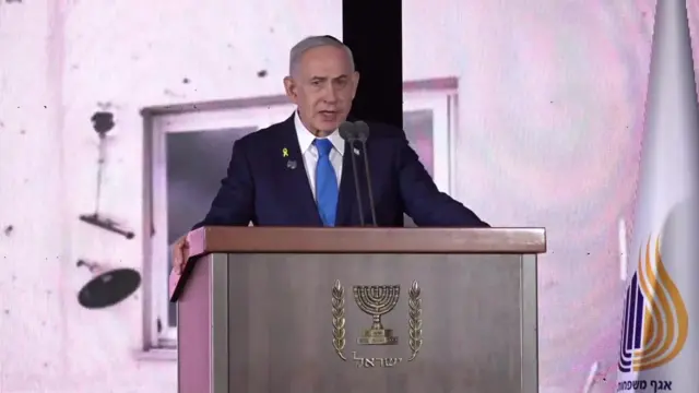 Netanyahu speaks into mic at wooden podium, wearing blue suit and tie