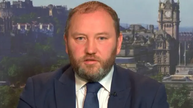 A headshot of Ian Murray wearing a suit against the background of Edinburgh city