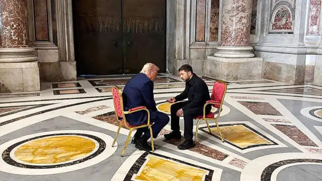 President Donald Trump and President Volodymr Zelesnky have their red chairs pulled close to one another and appear to be deep in conversation.