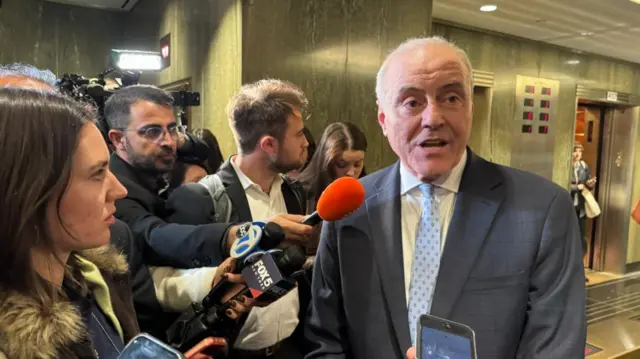 A group of reporters with microphones pointed at a man