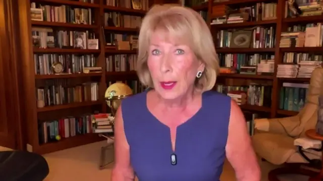 Former royal correspondent Jenny Bond in a blue dress, in the background is a wall covered in bookcases