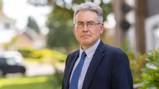 A headshot of Simon Foster against a blurred background